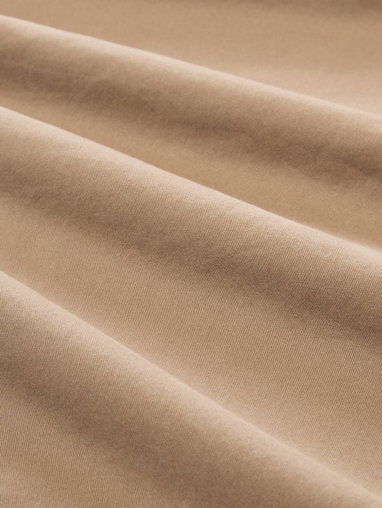 Gedetailleerd beeld van de stof van een beige chino met vouwen.