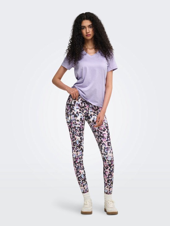 Model in paars sportshirt met V-hals en een veelkleurige legging met abstracte print. Ze houdt haar shirt op.