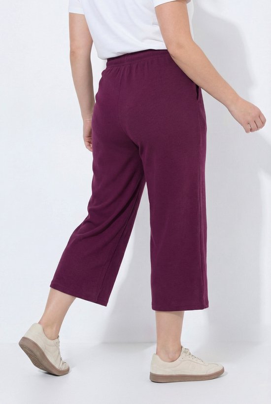 Achterkant model draagt een donkerrode sweatculotte met wafelstructuur en wijde pijpen.