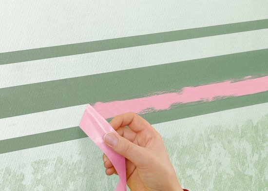 Hand trekt roze schilderstape los van een lichtgroene muur met groene strepen.