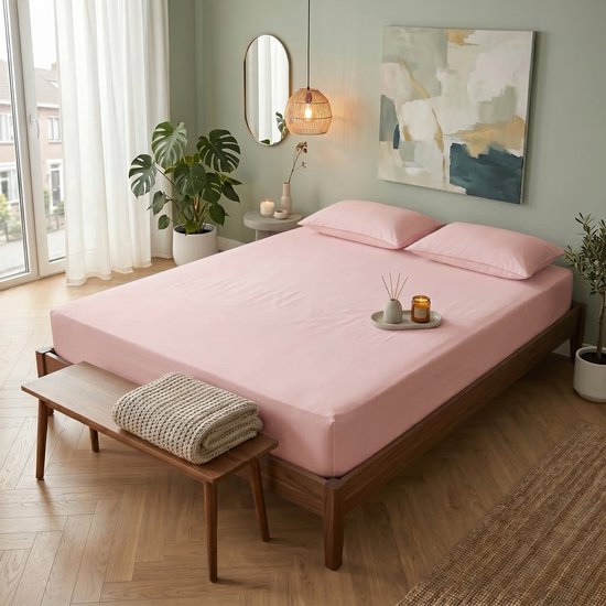 Un lit simple rose avec drap-housse et oreillers, à côté d'un banc en bois avec un jeté.