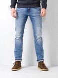 Man in een blauwe jeans met opgerolde broekspijpen en bruine schoenen. De jeans heeft een lichte wassing.