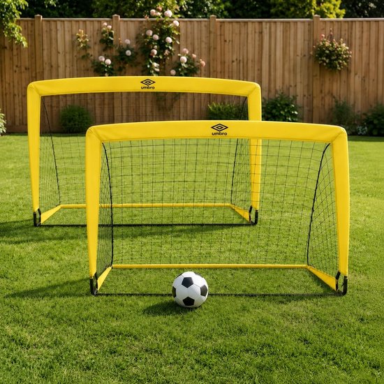 Twee gele Umbro voetbaldoeltjes op een groen gazon, met een voetbal ervoor.