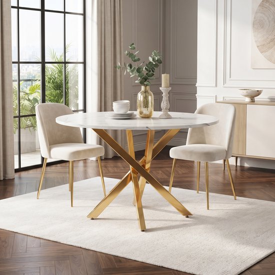 Ronde tafel met wit marmerlook blad en gouden X-poot, gefotografeerd met twee crèmekleurige stoelen.