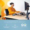 Een vrouw met bril en oranje trui gebruikt een documenthouder om te schrijven, zittend aan een bureau.