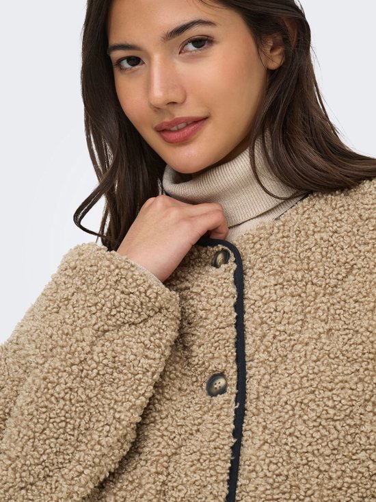 Model draagt een bruine teddy jas met zwarte biezen en knopen. Ze draagt ook een coltrui.