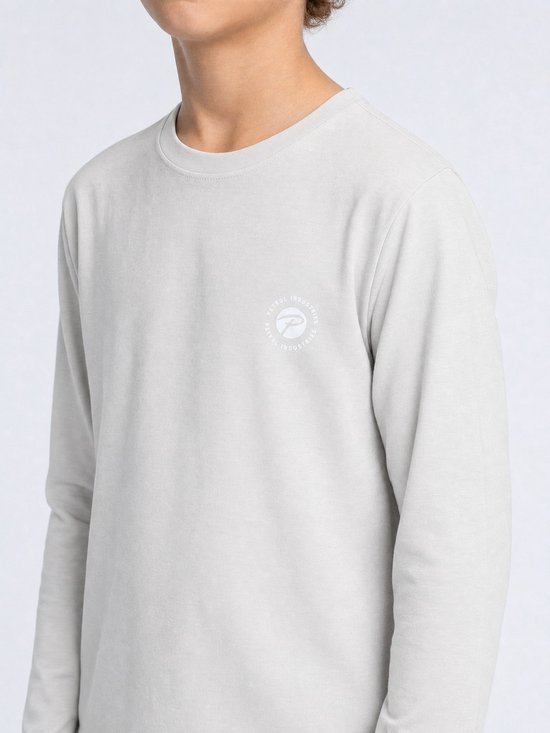 Close-up van een lichtgrijze jongens longsleeve met een rond logo op de borst.