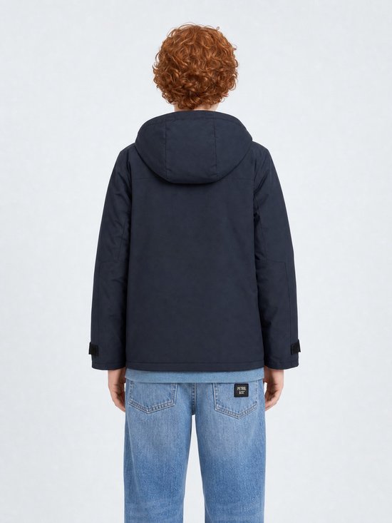 Jongen met krullend rood haar, achterkant van donkerblauwe jas en spijkerbroek.