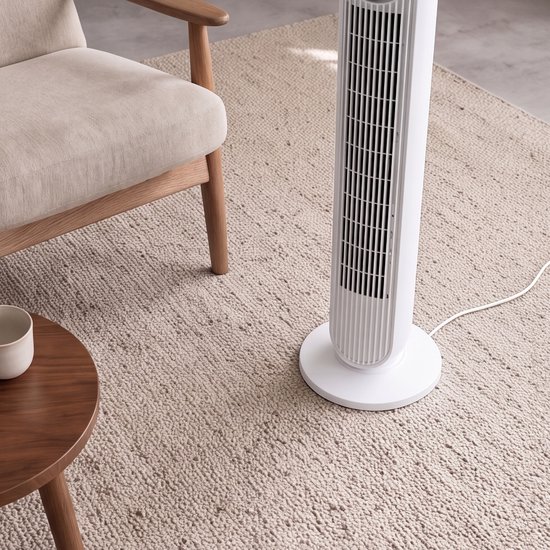 Witte torenventilator met geribbelde behuizing op een beige vloerkleed, naast een stoel.