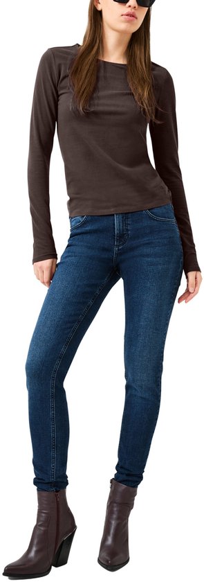 Vrouw met zonnebril in donkerbruine longsleeve, blauwe jeans en donkere enkellaarsjes.