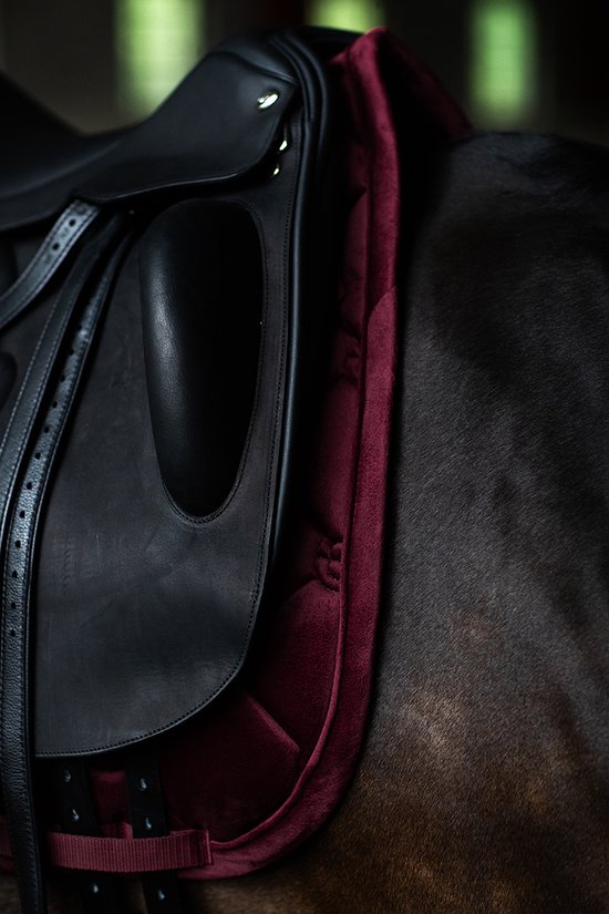 Donkerrode, gepofte dressuur deken onder een zadel op een paard.
