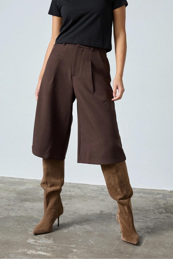 Bruine culottebroek met wijde pijpen, gedragen door een model met zwarte top en bruine laarzen.