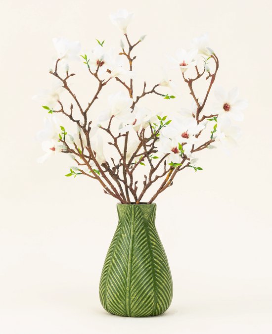 Een groen vaasje met ribbelpatroon, gevuld met een boeket witte magnoliabloemen en bruine takken.