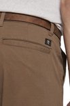 Achterzak van bruine chino broek met logo.
