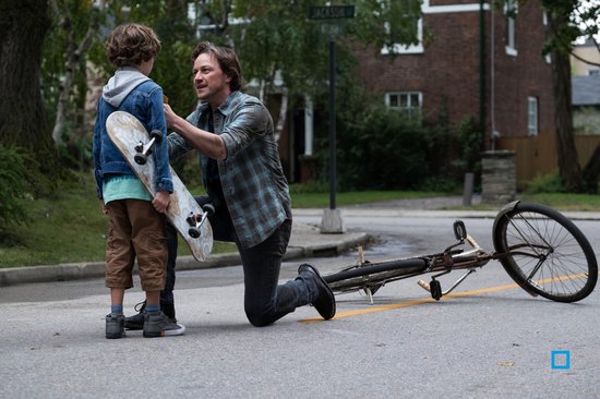 Man knielt voor een jongen, die een skateboard vasthoudt. Een fiets ligt omgevallen op de weg.