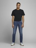 Man in zwart T-shirt en blauwe jeans met witte sneakers.