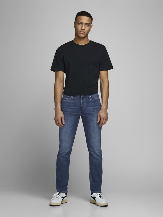 Man in zwart T-shirt en blauwe jeans met witte sneakers.