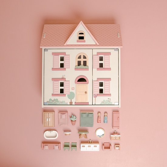 Houten poppenhuis met roze dak, met alle losse meubels en poppetjes eromheen op roze achtergrond.