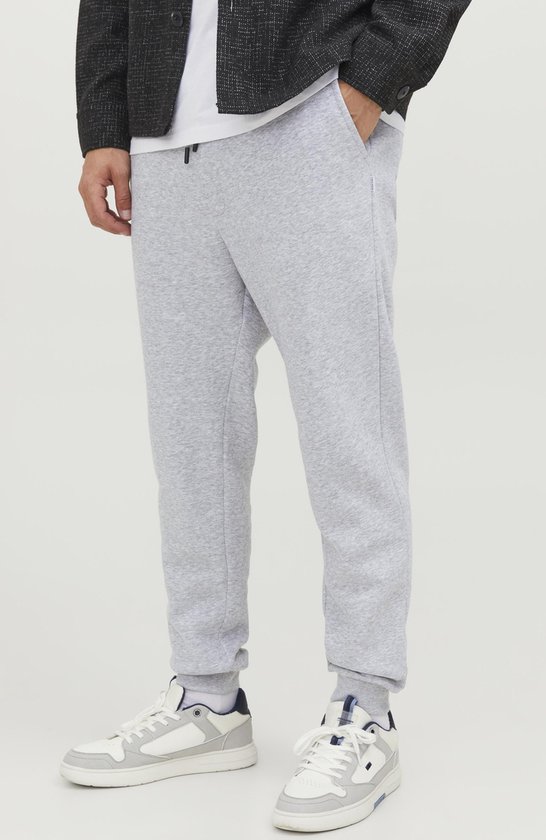 Man met lichtgrijze joggingbroek, wit T-shirt, zwart jasje en witte sneakers.