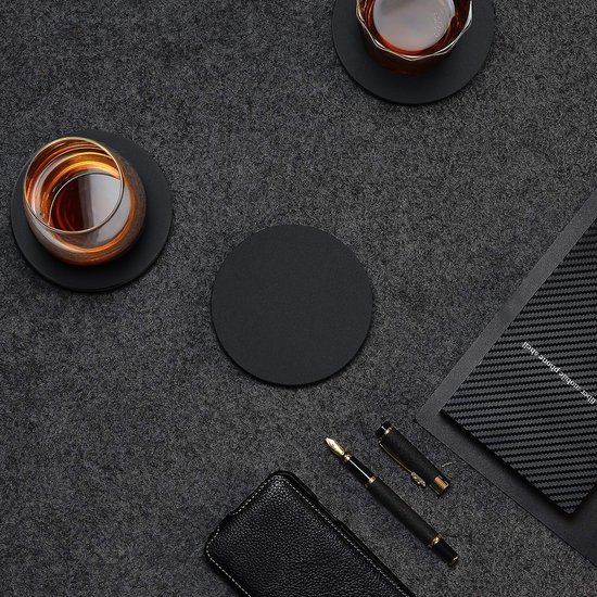 Sous-verre rond noir sur une nappe gris foncé, à côté de verres de boisson, d'un stylo et d'un carnet.