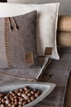 Bruin en beige kussen met een gestreept patroon, naast een gebroken wit kussen op een bruine plaid.