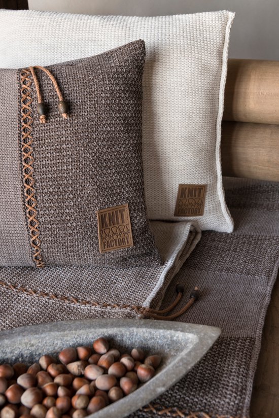Bruin en beige kussen met een gestreept patroon, naast een gebroken wit kussen op een bruine plaid.