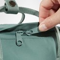 Hand aan de ritstrekker van een groene Fjällräven Kånken rugzak.