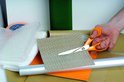 Handen gebruiken oranje Fiskars schaar om noppenfolie te knippen.