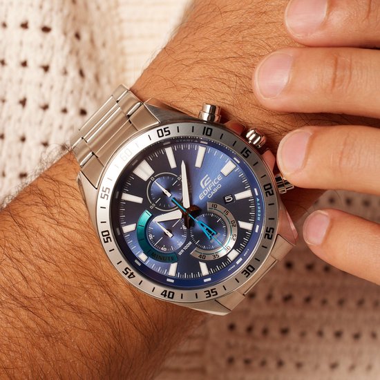 Detailopname van herenhorloge met zilverkleurige metalen band en blauwe wijzerplaat met chronograaf.