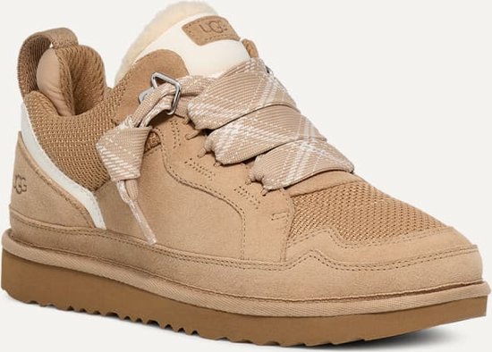 Beige UGG sneaker met bruine zool, schapenwollen voering en stoffen veters met ruitpatroon.
