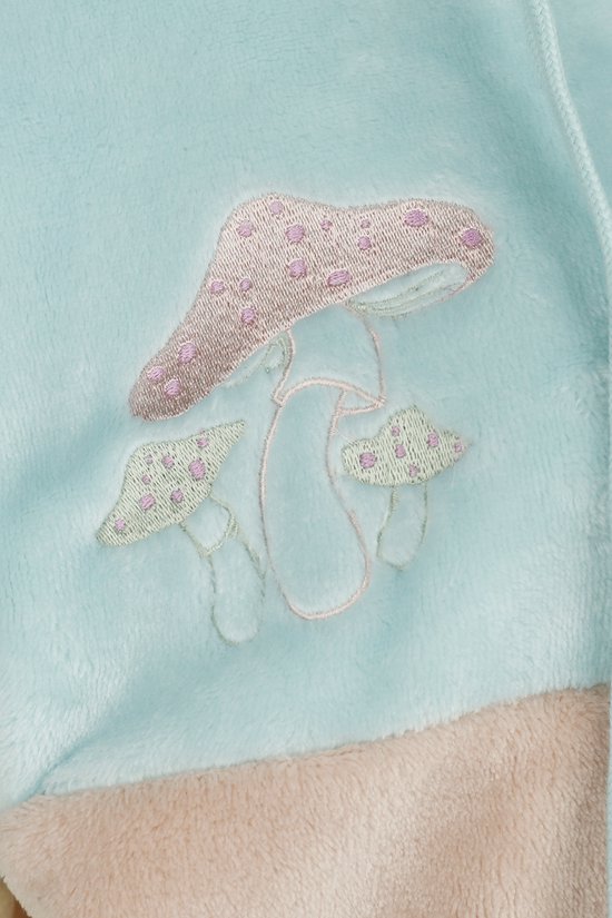 Close-up van de turkooizen teddy stof met broderie van roze en lichtgroene paddestoelen.