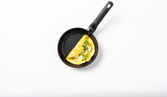 Zwarte koekenpan met een omelet, gegarneerd met groene kruiden.