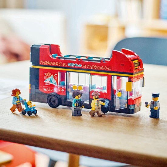 Rode LEGO dubbeldekker bus met "City Tour" tekst, staand op een tafel met minifiguren van passagiers en een chauffeur.