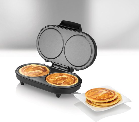 Open dubbele pancakemaker met 2 gebakken pancakes, naast een stapel pancakes op een wit bord.