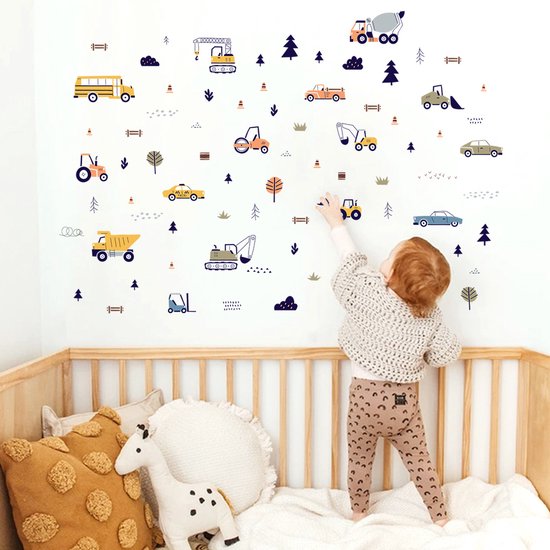 Chambre de bébé avec des autocollants muraux de véhicules et d'arbres. Un enfant en pantalon brun et gilet blanc tend la main vers un autocollant de bus scolaire jaune.