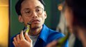 Man met bril trimt zijn snor en baard met een groene en zwarte Philips OneBlade, kijkend in de spiegel.