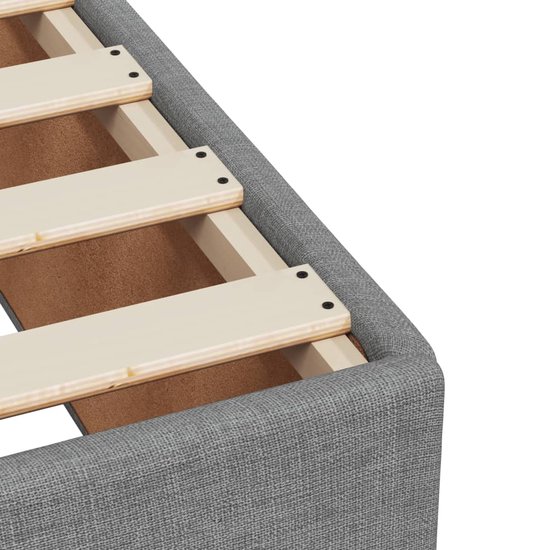 Détail du revêtement en tissu gris clair d'un sommier avec lattes en bois.