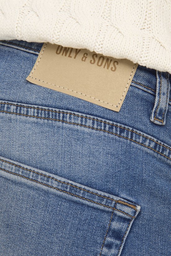 Close-up van het bruine lederen logo 'ONLY & SONS' op de achterkant van een spijkerbroek.