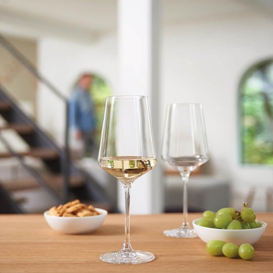 Un verre de vin blanc sur une table en bois, avec un cadre domestique en arrière-plan.