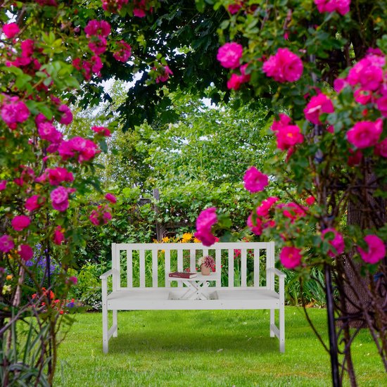 Witte houten 3-zits tuinbank met inklapbaar tafeltje in een tuin vol roze bloemen.