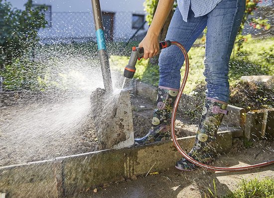 Een persoon met GARDENA Comfort EcoPulse spuitpistool, sproeit een spade af in de tuin.