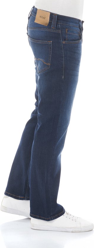 Man in profiel, draagt een donkerblauwe bootcut jeans van Mustang met witte sneakers.