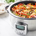 Close-up van een roestvrijstalen multicooker met een wokgerecht van garnalen en groenten.