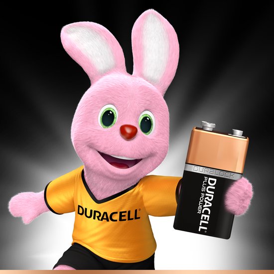 Roze Duracell konijn met groene ogen en rode neus, draagt geel shirt met Duracell logo. Houdt een Duracell 9V batterij vast.