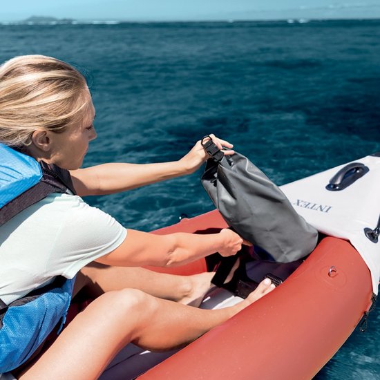Vrouw met blauw reddingsvest stopt grijze drybag in rode en witte Intex kajak.