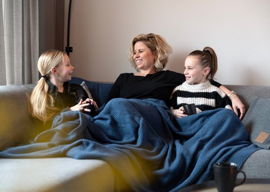 Moeder met twee dochters onder een blauwe deken op een grijze bank.