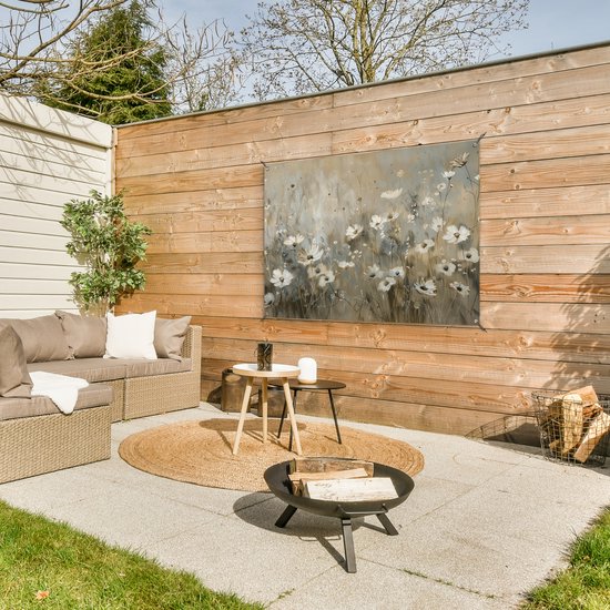 Een tuinposter met een schilderij van witte bloemen met grijze en beige tinten, opgehangen aan een houten schutting.