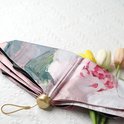 Gevouwen paraplu met roze pioenrozen schilderijprint, met gouden knop en handvat, op een wit gestructureerd oppervlak.