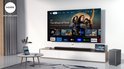 Zwarte soundbar en subwoofer naast een tv die op een laag meubel staat. Een laptop en tablet zijn ook zichtbaar.