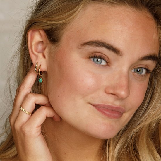 Close-up van een vrouw met blonde haren, met gouden oorbellen met turkoois en twee gouden ringen.